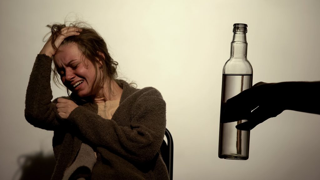 Alcoholic woman suffering strong withdrawal, male hand holding bottle of vodka